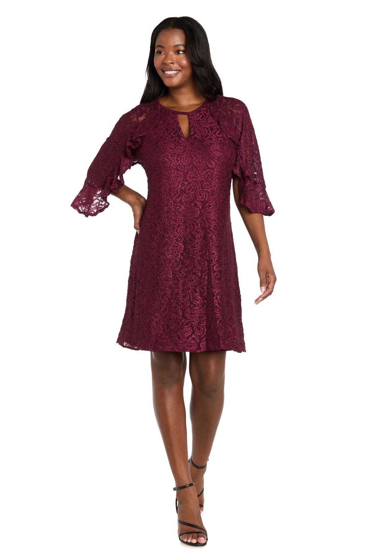 A woman wearing the R&M Richards 4226 Short Lace Semi-Formal Dress with a knee-length a-line silhouette, burgundy glitter lace, three-quarter bell sleeves, and black strappy heels stands against a white background.